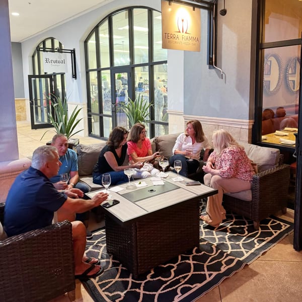 Six people enjoying drinks and conversation on a patio with Terra Fiamma signage visible.
