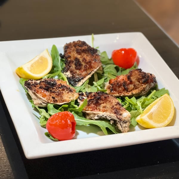 Four baked clams on a bed of arugula, garnished with lemon wedges and cherry tomatoes.