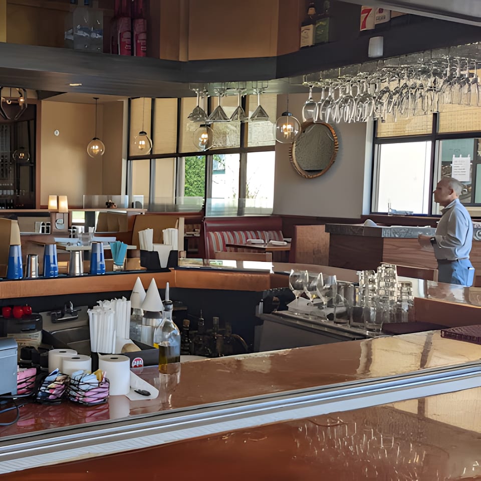A Terra Ristorante & Bar interior with a bar counter, hanging wine glasses, and a person standing.