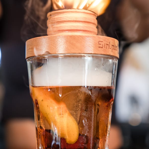 A smoked cocktail with an orange peel, topped with a wooden smoker and flame.