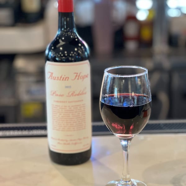 A bottle of Austin Hope Paso Robles red wine next to a glass filled with red wine.